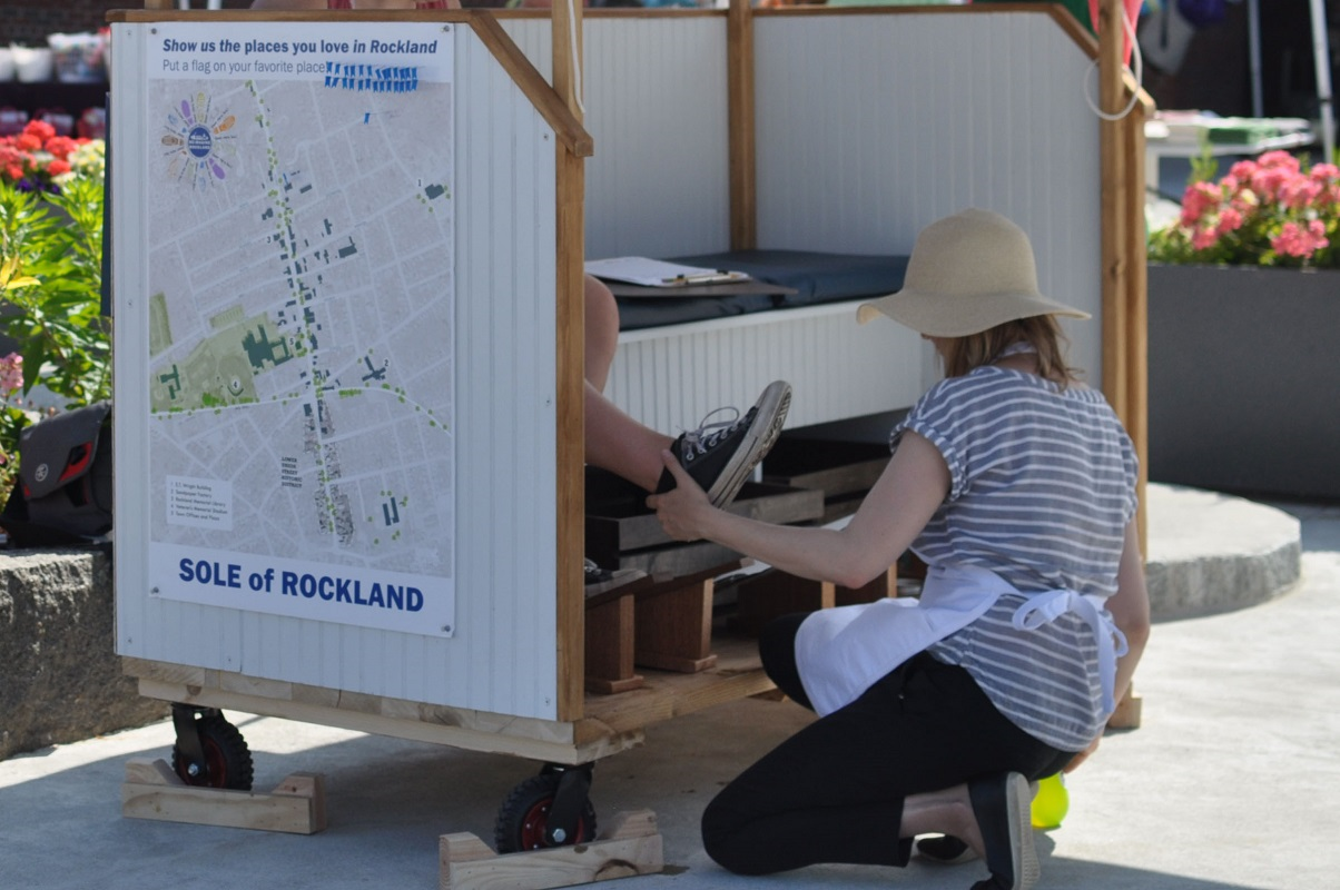 Sole of Rockland At a replica shoeshine cart with "Sole of Rockland" written on it, a woman prepares to create a shoeprint.