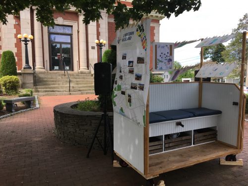 Image shows portable shoeshine cart with watercolor shoeprint paintings hanging on it