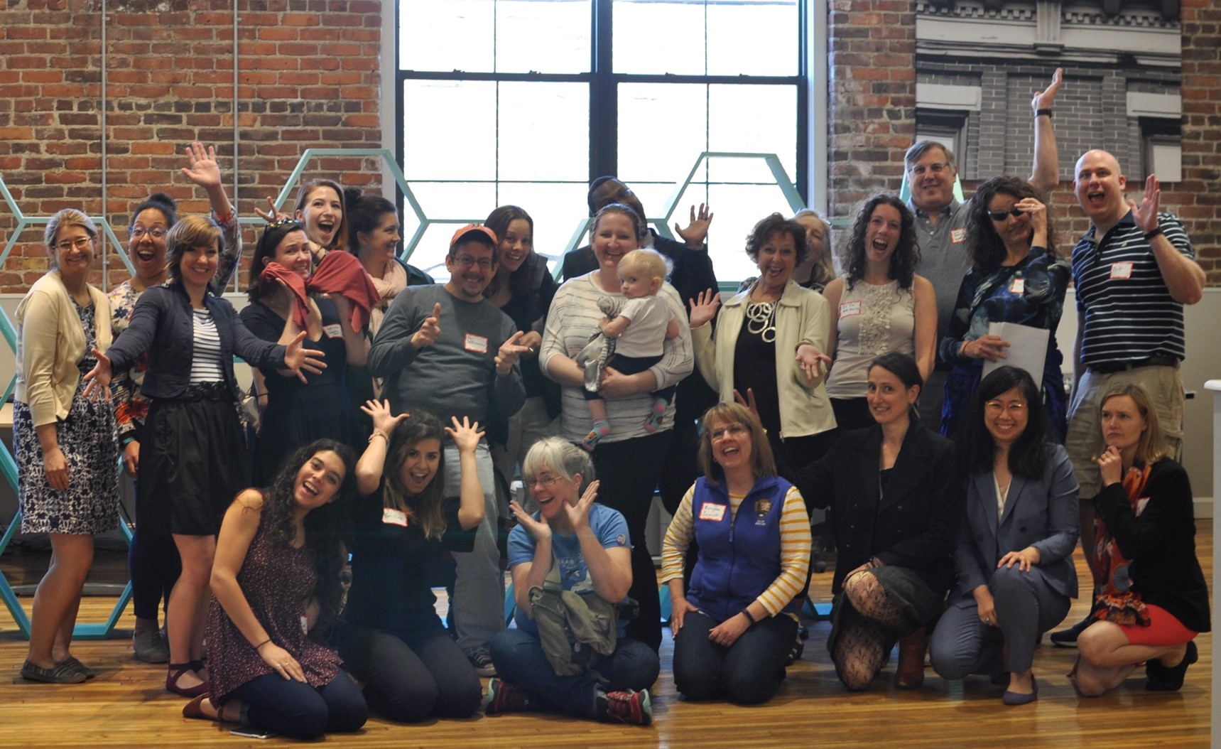 A group of people who attended an MAPC Creative Placemaking workshop smile and wave at the camera.