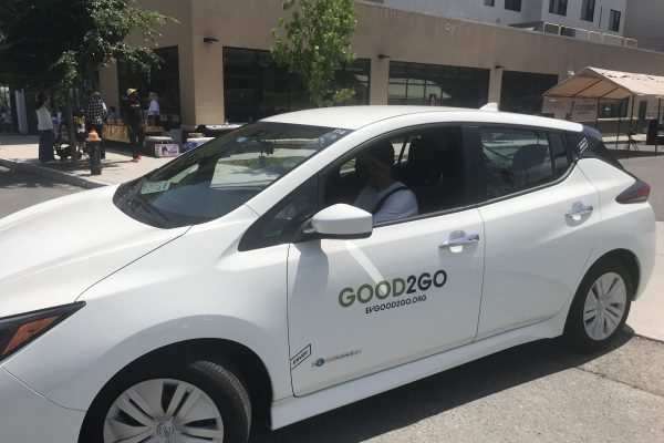 A man sits in shadow inside a white Good2Go electric car sharing vehicle.
