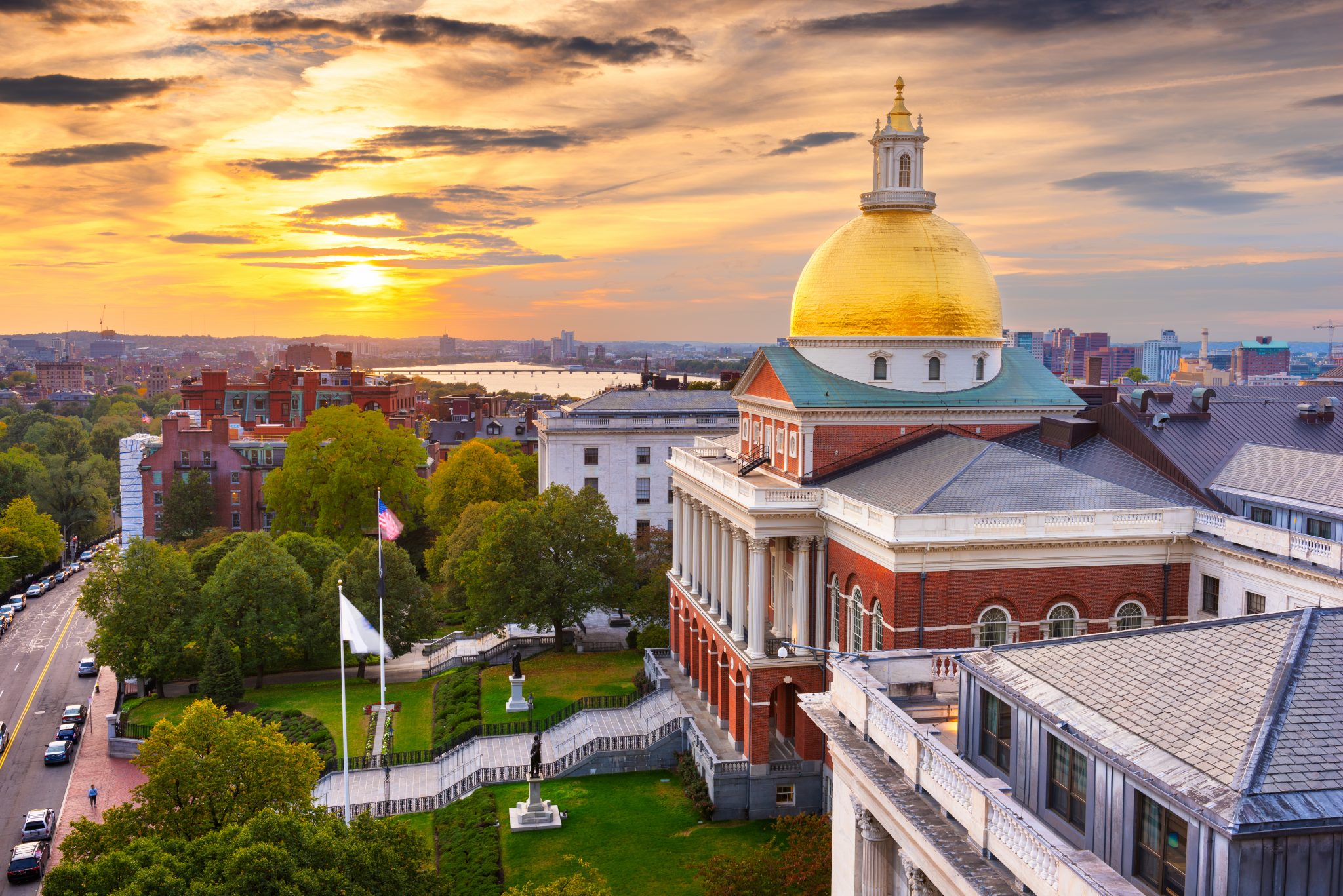 Boston, Massachusetts, USA cityscape with the State House Photo is a somewhat aerial shot of one side of the Massachusetts State House with the sun setting or rising behind it.