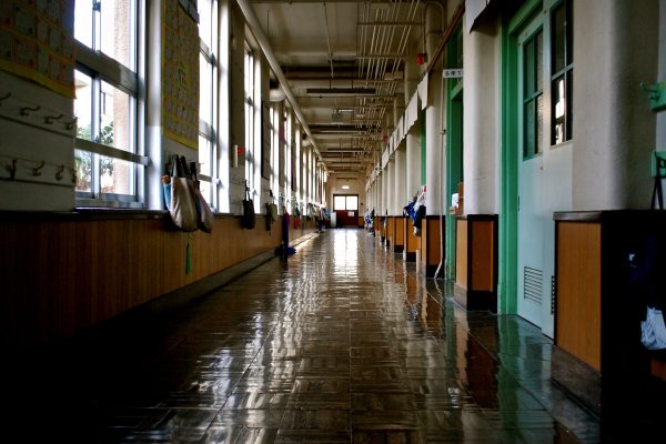 A dimly lit corridor in a school. Windows line the left side and doors on the right.