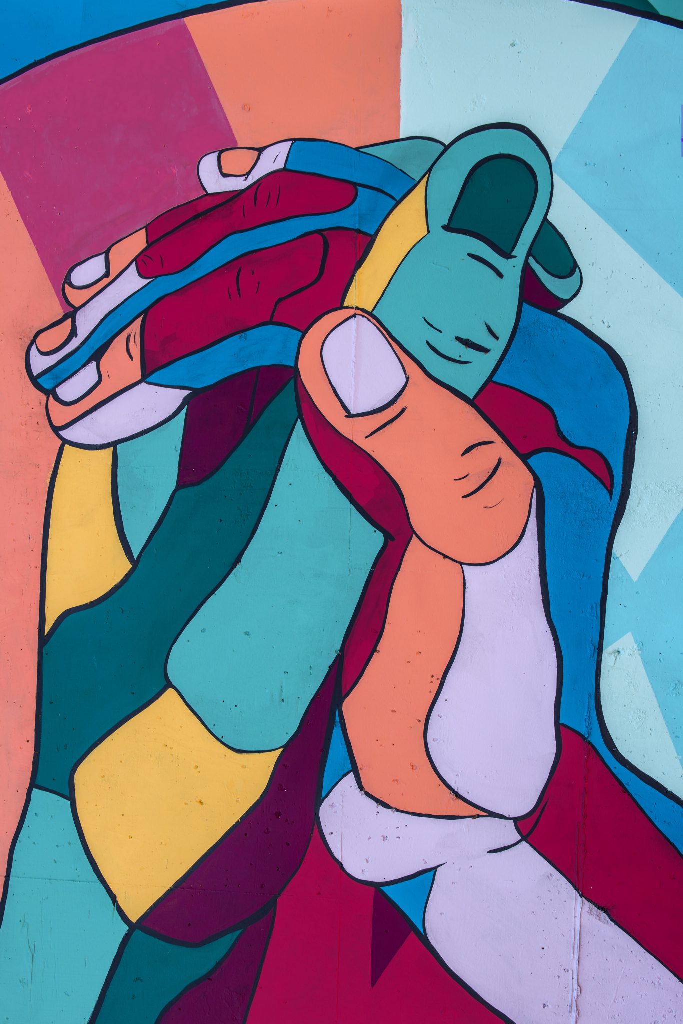 Photo of a painted wall mural which depicts two hands held together. The image is depicted in a mosaic-style of colorful blocks such as: bright and dark teal, light and medium blue, salmon, magenta, and dark purple, as well as yellow.