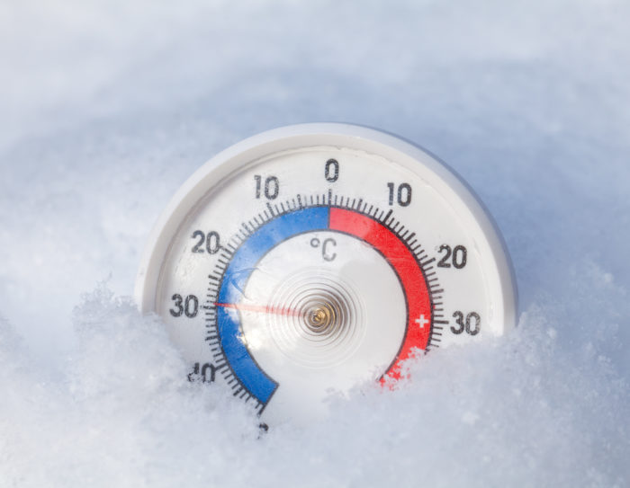 Frozen thermometer shows minus 29 Celsius degree extreme cold wi Image is of a round, white thermostat that has red and blue circle in the middle, in snow. The temperature on it reads about 30 degrees Celsius.