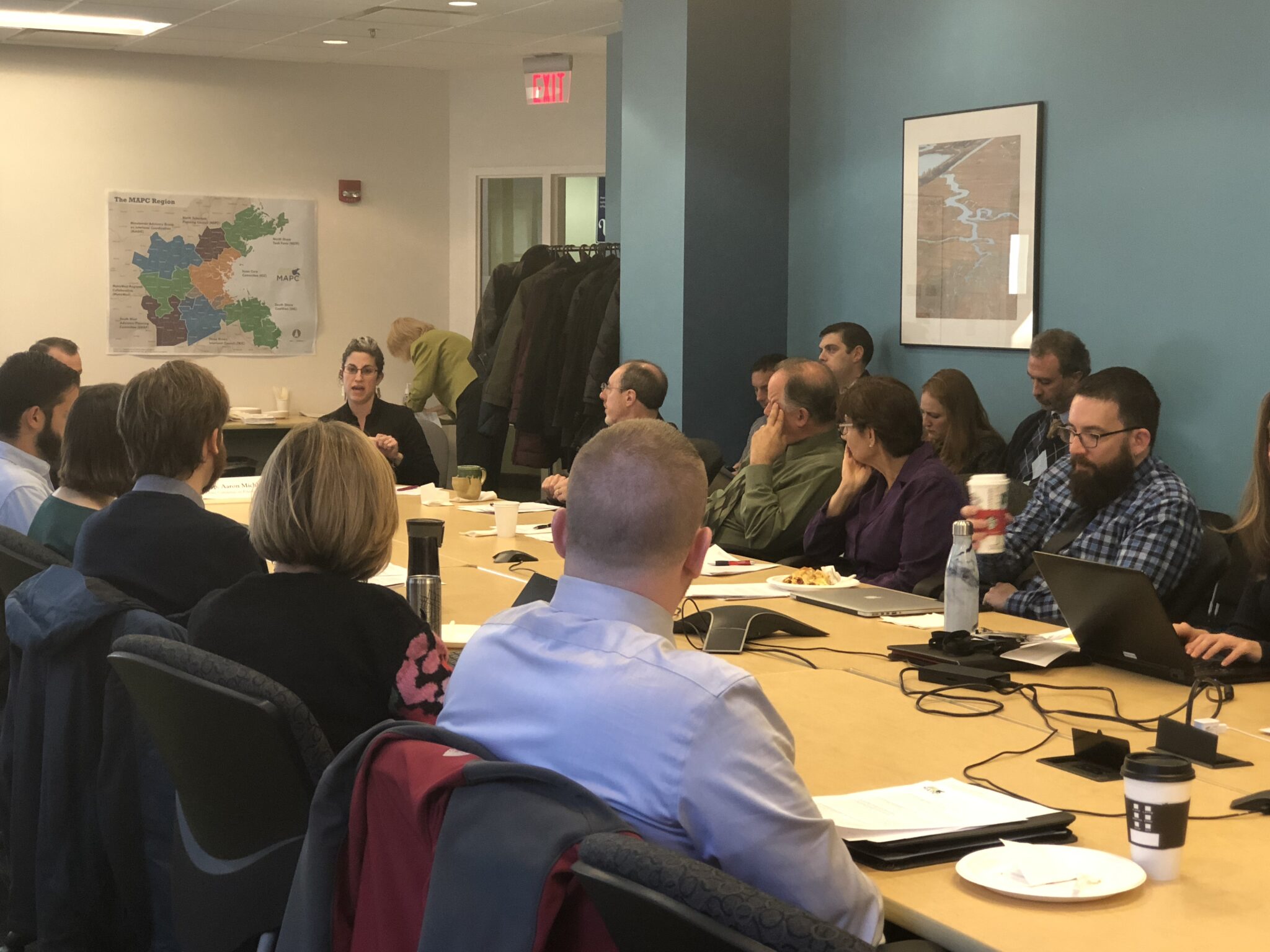 Many people sitting in chairs at a long table. People are sitting on both sides looking at one person speaking.