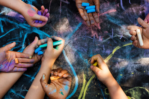 Children's hands coloring with chalk on a black background.