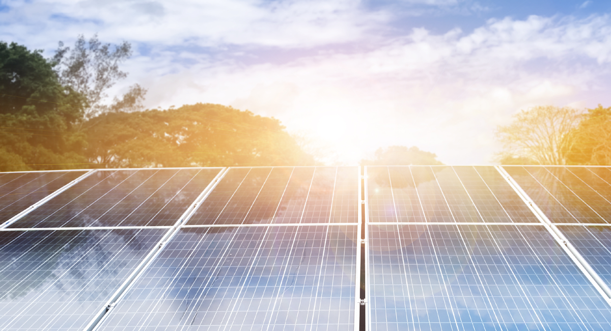 Photo of solar panels with a setting sun and a blue sky with some clouds in the background.