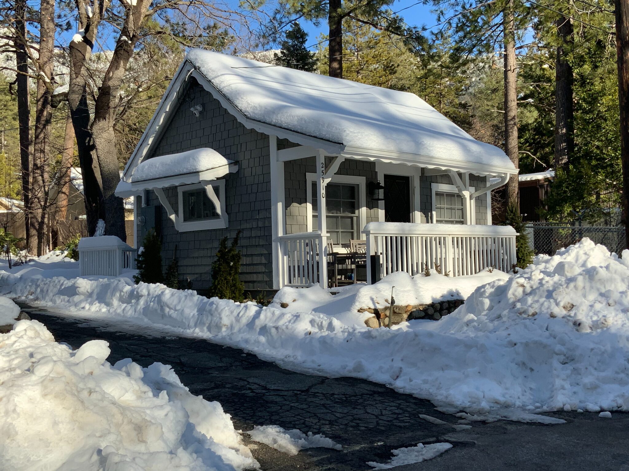A photo of a small, accessory dwelling unit-type home in Massachusetts. The home is gray and snow-covered. A window on the side of the home, a small front porch, and two additional windows are visible.