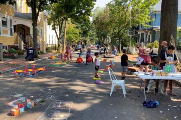 A photo of a block party in Cambridge, MA. Children play on a closed street with a table and activities set up.