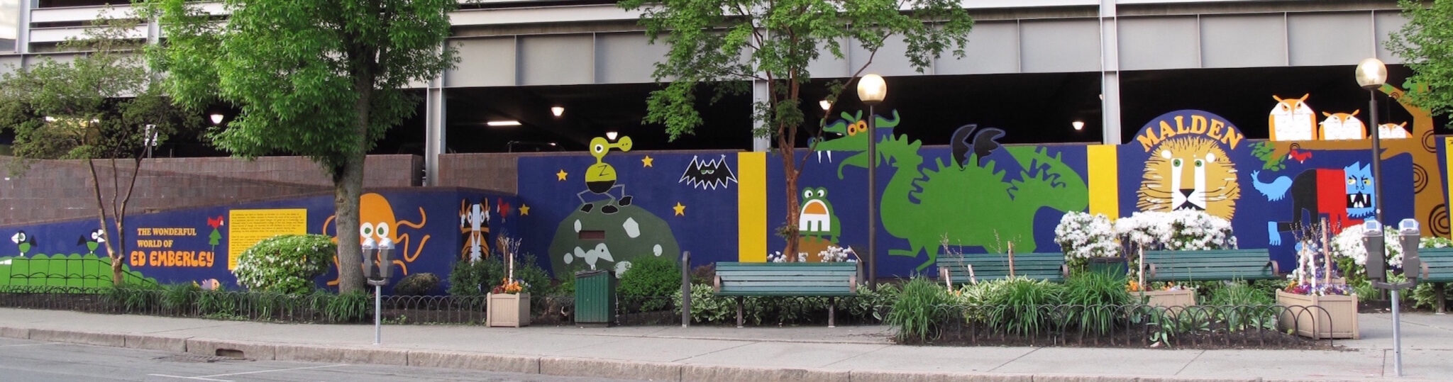 A mural with a blue background with animals including a lion, octopus, dragon, along a small garden with trees and benches.