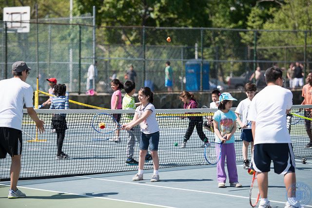 Young kids on a blue and green tennis court with two tennis instructors at Amerige Park.