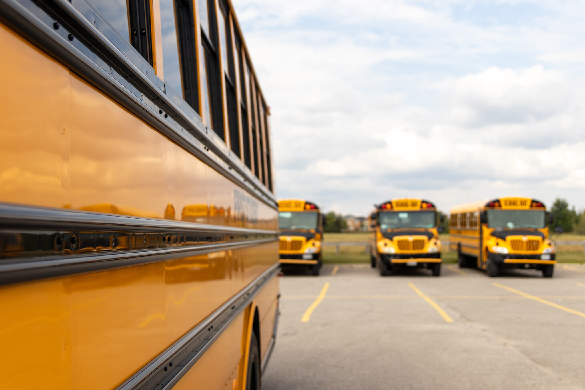 Side view close-up of yellow school bus - parked - sunny day with clouds in sky. Taken in Toronto, Canada. Side view close-up of a yellow school bus - parked with other yellow school buses parked in the background - sunny day with clouds in sky