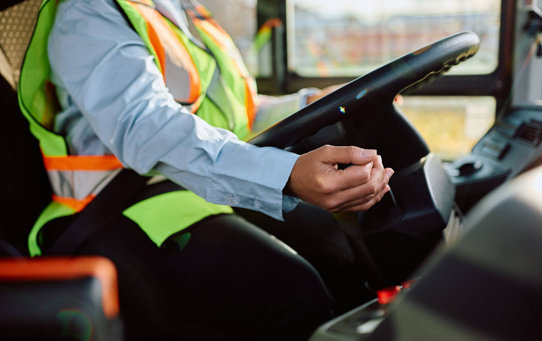 AdobeStock_591649264 (1) - crop Close up of a school bus driver wearing a green and orange safety vest sitting in the drivers seat driving.