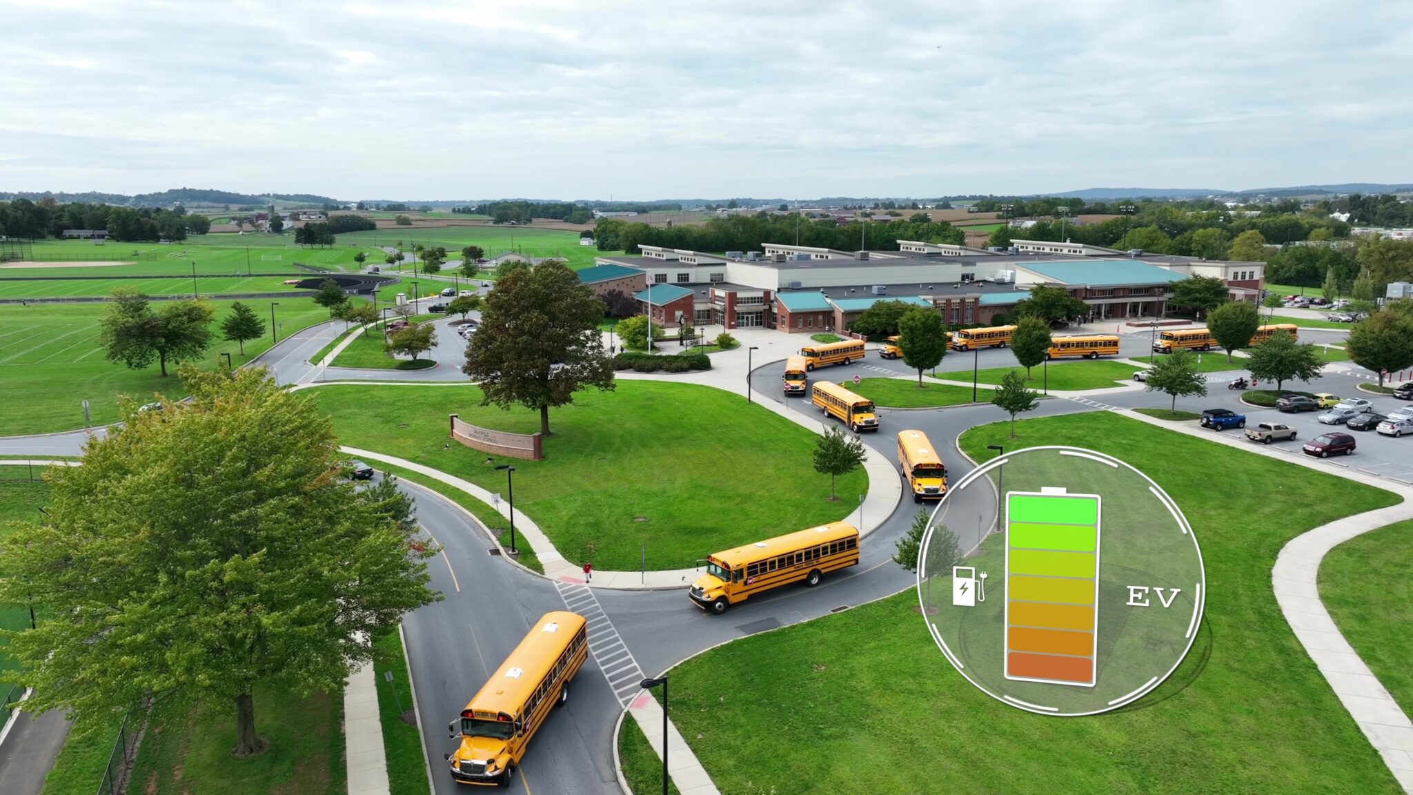 Electric buses with battery status icon. Aerial of eco-friendly public transport of students in USA. EV graphic charging icon with yellow buses leaving American school Electric buses with battery status icon. Aerial of eco-friendly public transport of students in USA. EV graphic charging icon with yellow buses leaving a school parking lot.