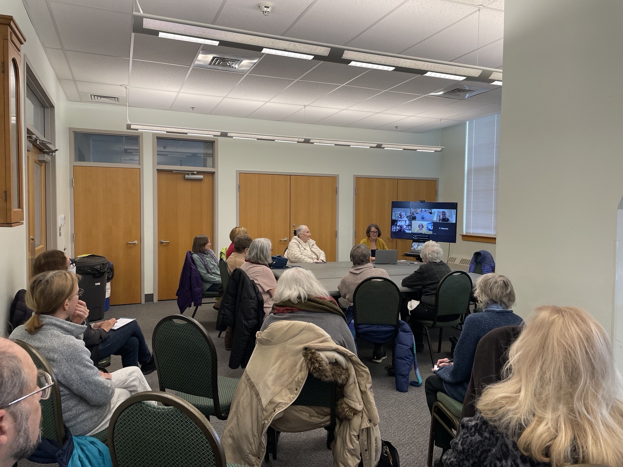 Town of Concord projec A room full of people sitting in chairs and facing a tv screen that has a zoom call on it.