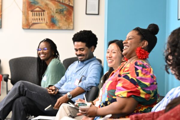 Four participants during the Community Engagement Convening in June 2025 are pictured seated laughing and smiling.