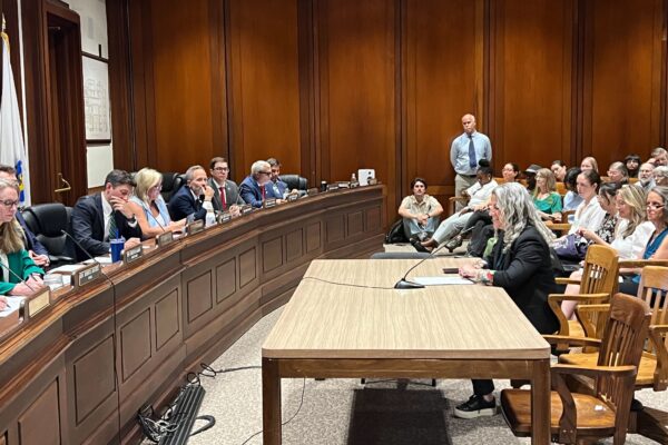Acting Executive Director Lizzi Weyant is pictured seated at a large table as she testifies at the State House in support of the Environmental Bond Bill.