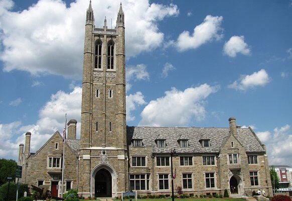 A photo of Norwood's Town Hall. The large beige stone building has a tower with two spires and two long windows visible.