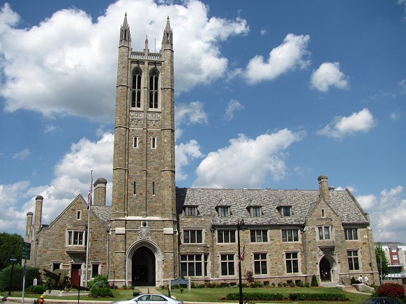 A photo of Norwood's Town Hall. The large beige stone building has a tower with two spires and two long windows visible.