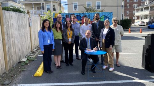 Mayor Dominick Pangallo is pictured at a small table with Lizzi Weyant to his left and a larger group of people standing behind. Photo was taken in a parking lot in Salem.