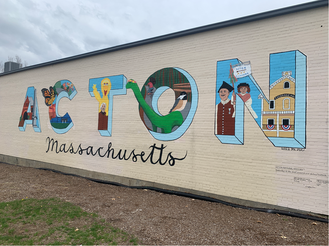 a mural of the words “ACTON, Massachusetts.” The 3-dimensional block lettering for Acton have images of important elements of Acton history and culture including The Acton Public Library, Acton Arboretum, Caroll Swinney and Big Bird, The Bruce Freeman Rail Trail and Bessie the dinosaur, the Acton Minutemen and the Exchange Hall in South Acton.