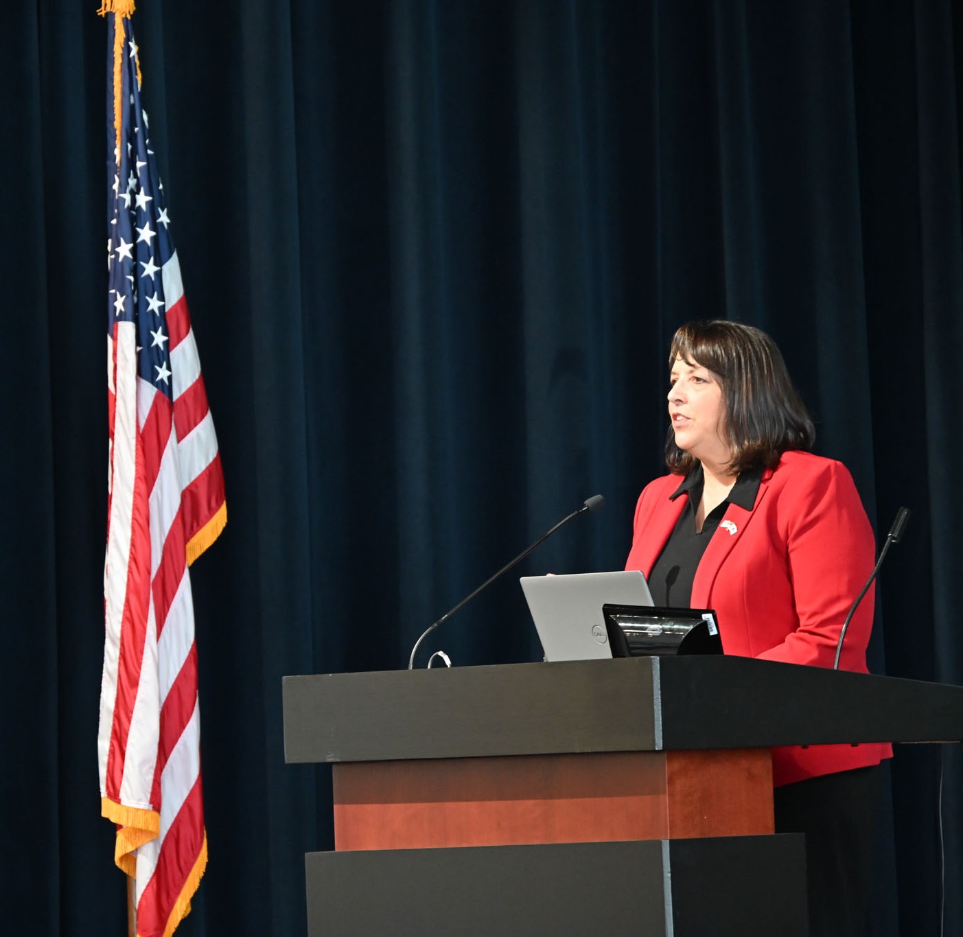 DSC_1231 Lt. Governor Kim Driscoll is pictured standing at a podium and looking outwards to attendees at the 2025 MARPA conference. An American Flag stands to her right.