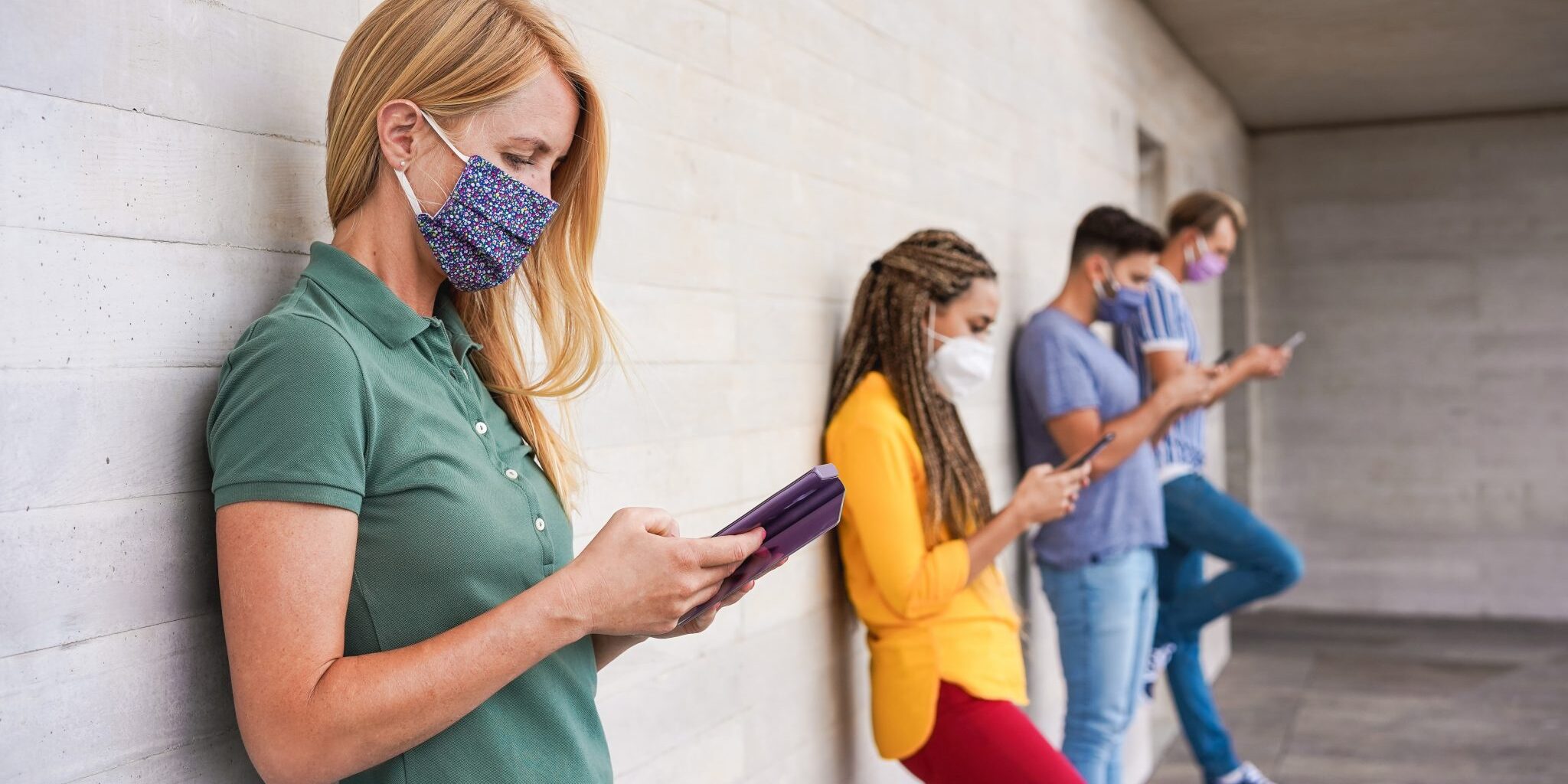 Young people wearing face safety masks using smart mobile phones while keeping social distance during coronavirus time - Technology and covid-19 spread prevention concept - Focus on blond girl hand