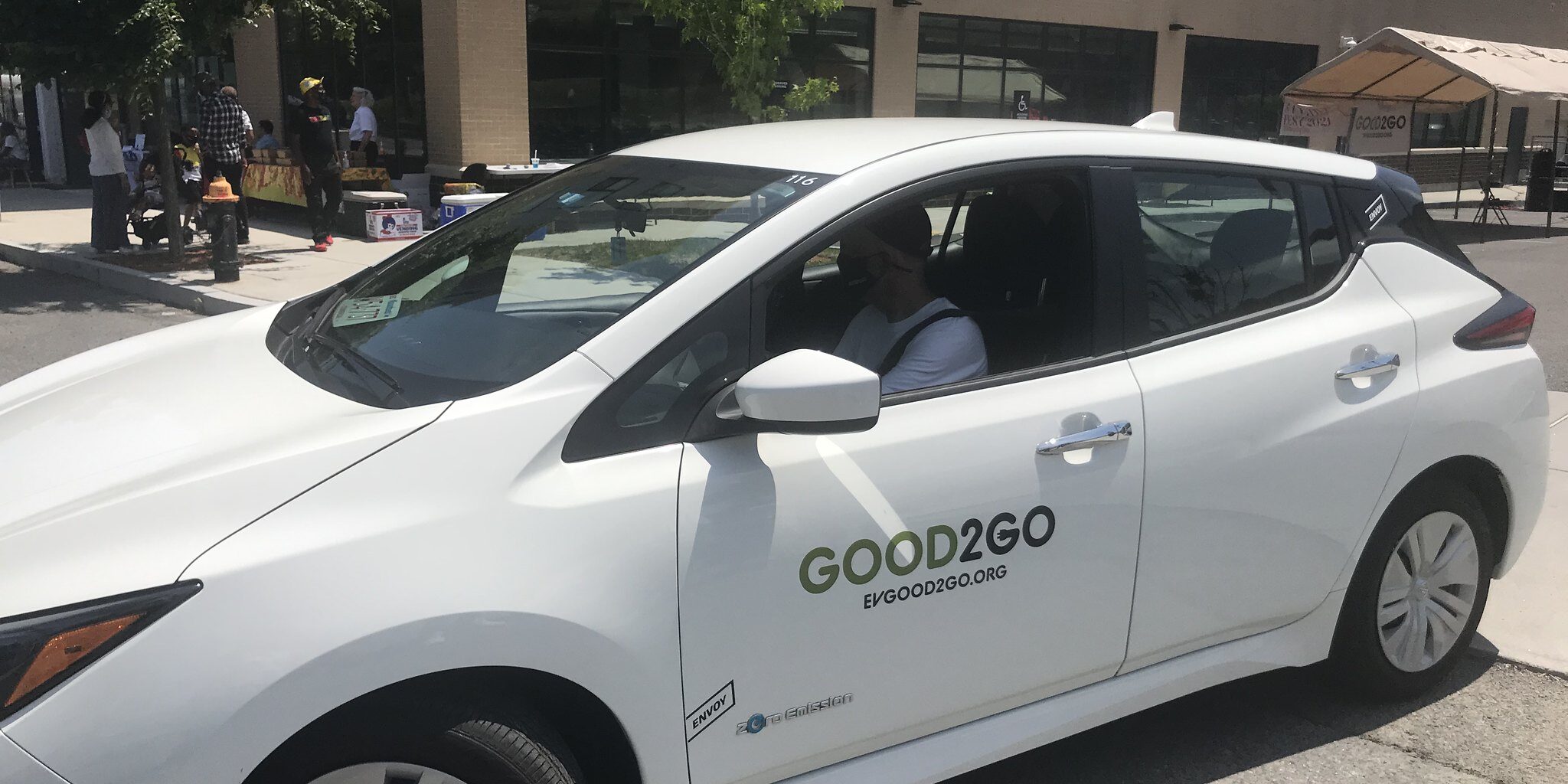 A man sits in shadow inside a white Good2Go electric car sharing vehicle.