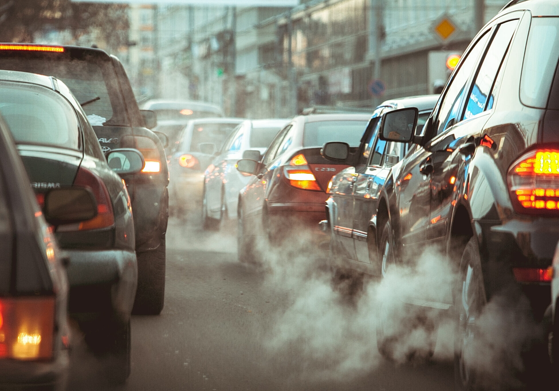 strong car traffic jams in the city View from behind of many cars driving down the road while their exhaust pipes are emitting smoke or pollutants.