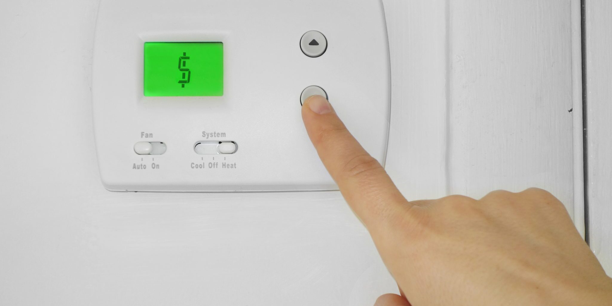 Person adjusting a wall thermostat with dollar sign symbol on the display