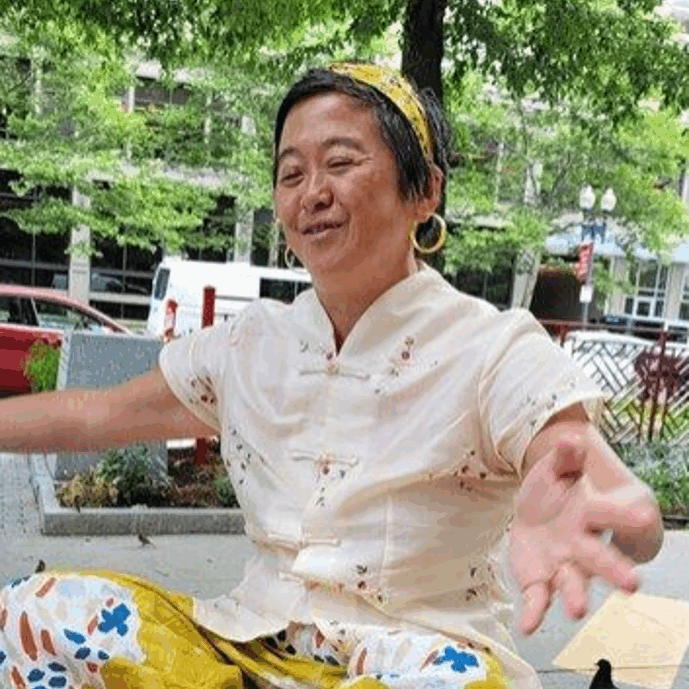 Heang_Rubin A photo of Heang Rubin sitting crossed leg on the ground, with eyes closed, and both arms outstretched.